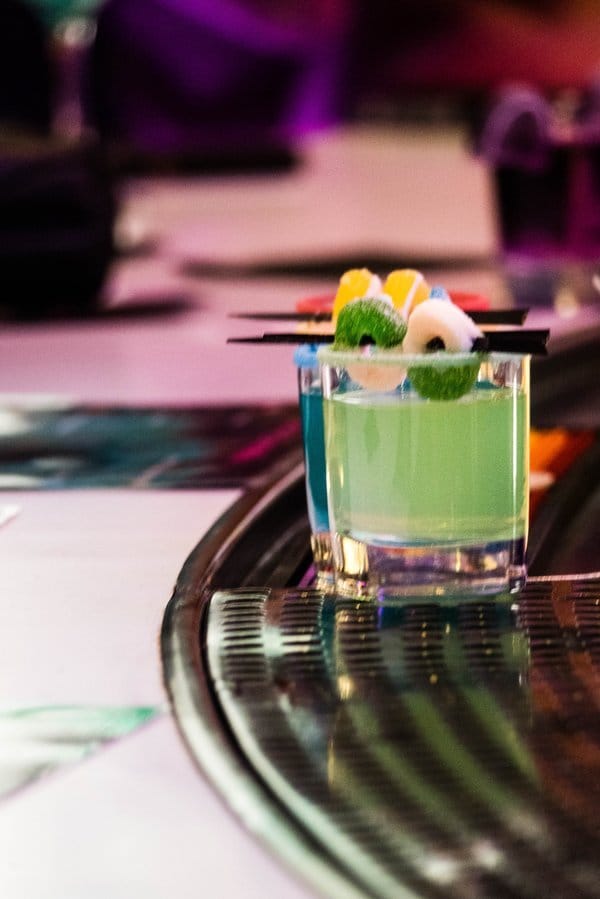 Two green cocktails with lemon garnish on a bar.