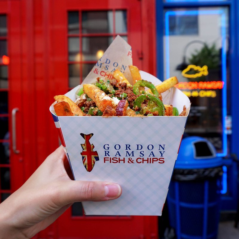 Gordon Ramsay Fish & Chips takeout container held by a hand.