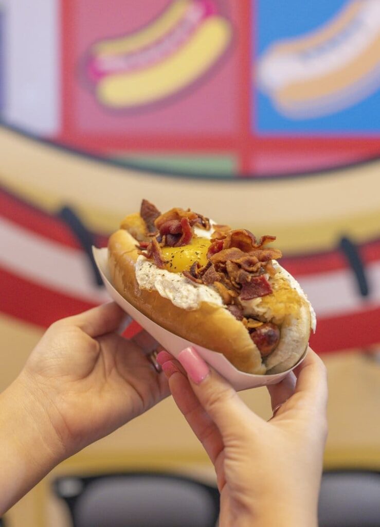 Loaded hot dog held in hands.