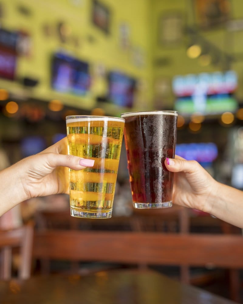Two hands toasting glasses of beer in a bar.