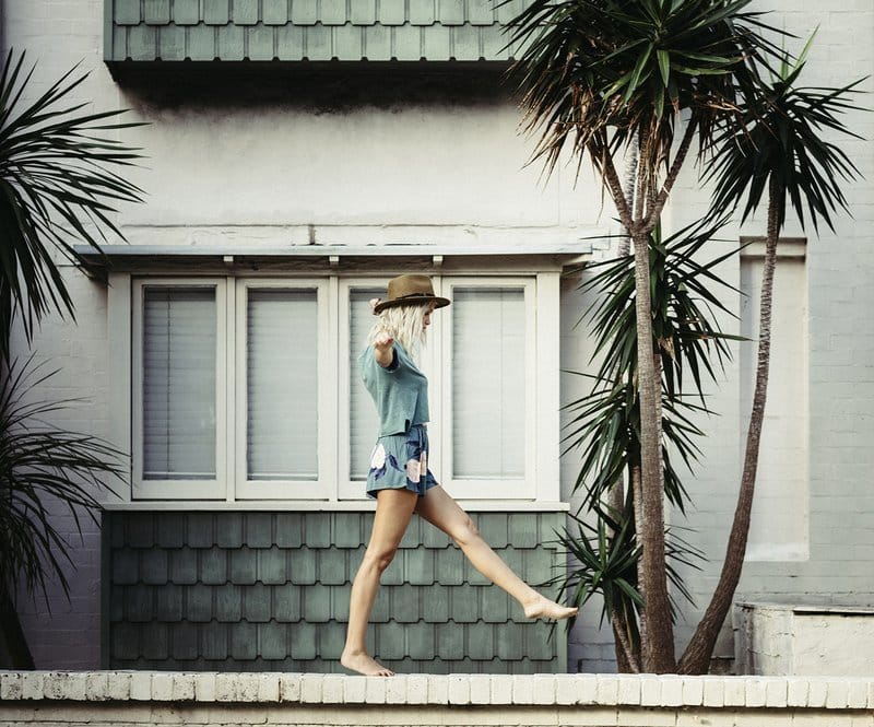 Person walking barefoot on a wall by a house with palm trees.