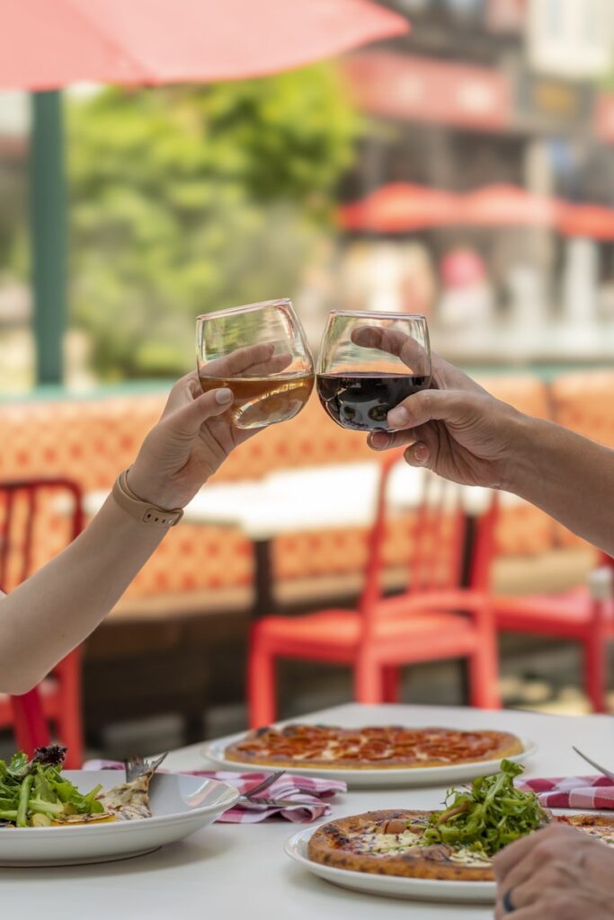 Two hands toasting with wine glasses outdoors.