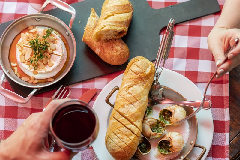 French cuisine: Escargots, baked brie, and baguette on a red checkered tablecloth.