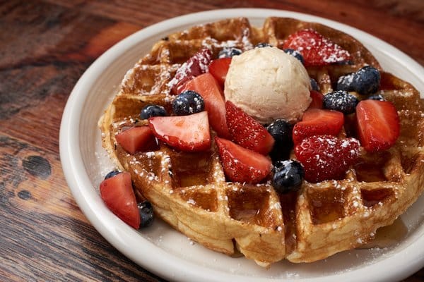 Waffle topped with strawberries, blueberries, and ice cream.