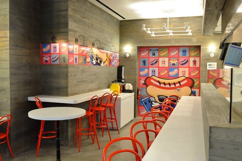 Modern hot dog restaurant interior with red stools.
