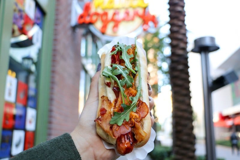 Gourmet hot dog with arugula and toppings.