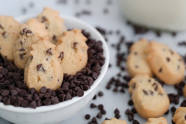 Chocolate chip cookie bites in a bowl surrounded by chocolate chips.