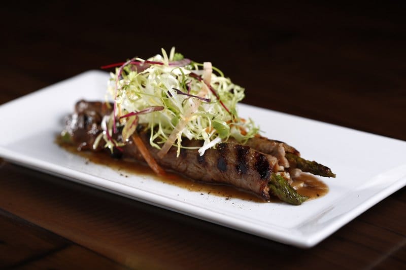 Beef rolls with asparagus and salad on a white plate.