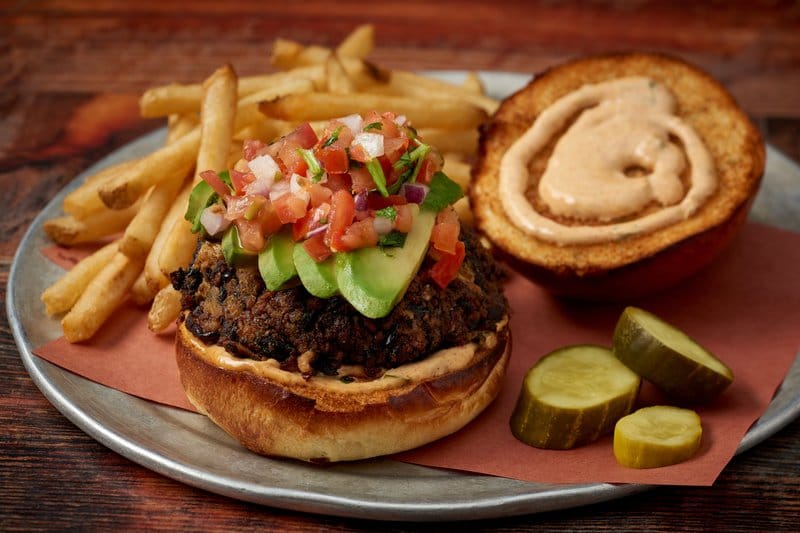Open black bean burger with avocado, pico de gallo, fries, and pickles.