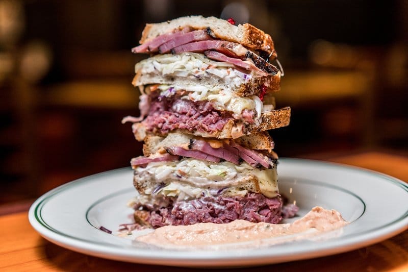 Tall stacked pastrami sandwich on a plate.
