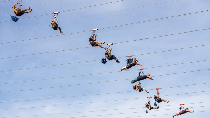 People ziplining against a blue sky.