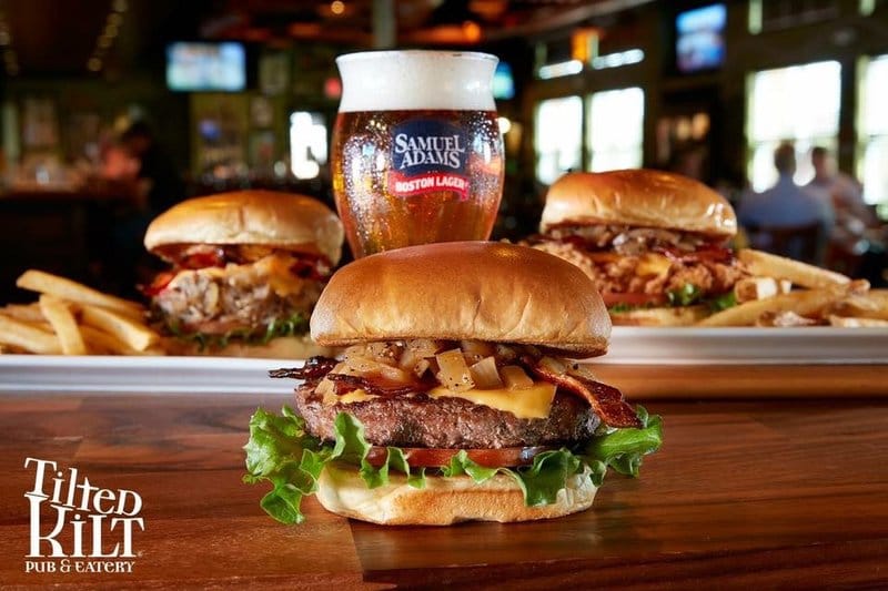 Three hamburgers and a beer on a wooden table in a restaurant.