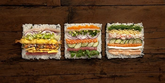 Three square sushi "sandwiches" on a wooden surface.