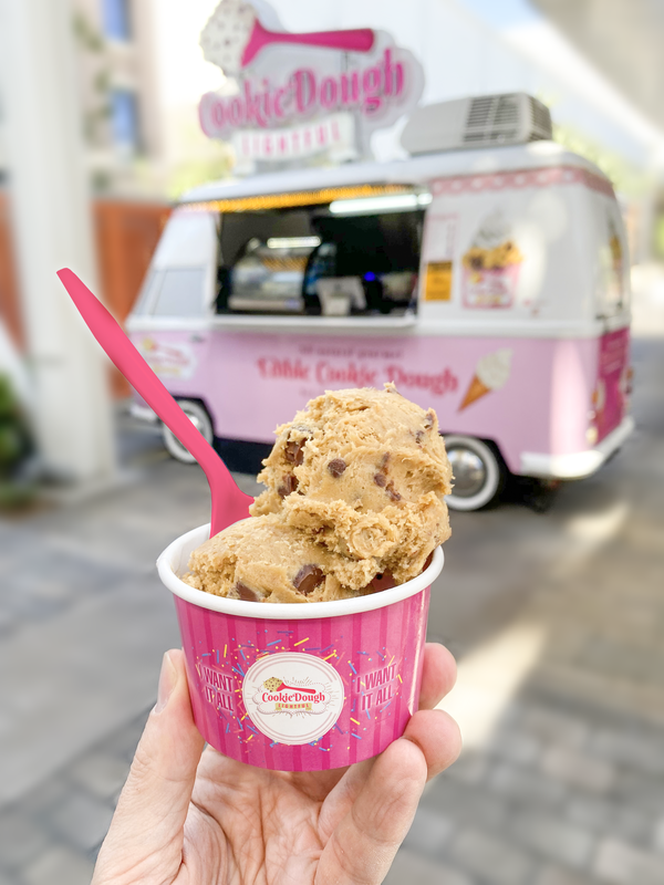 Cookie dough in pink cup with matching spoon, food truck in background.